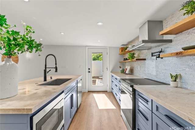 kitchen with wall chimney exhaust hood, appliances with stainless steel finishes, open shelves, and a sink