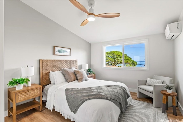 bedroom featuring a wall unit AC, a ceiling fan, vaulted ceiling, wood finished floors, and baseboards