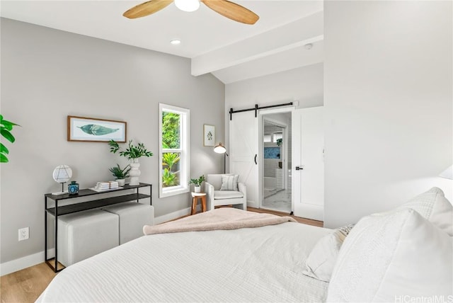 bedroom featuring baseboards, light wood-style flooring, lofted ceiling with beams, and a barn door