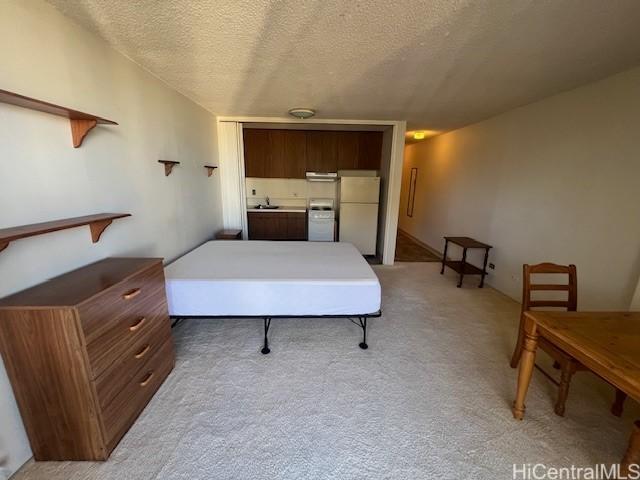 bedroom with light colored carpet, a textured ceiling, and white fridge