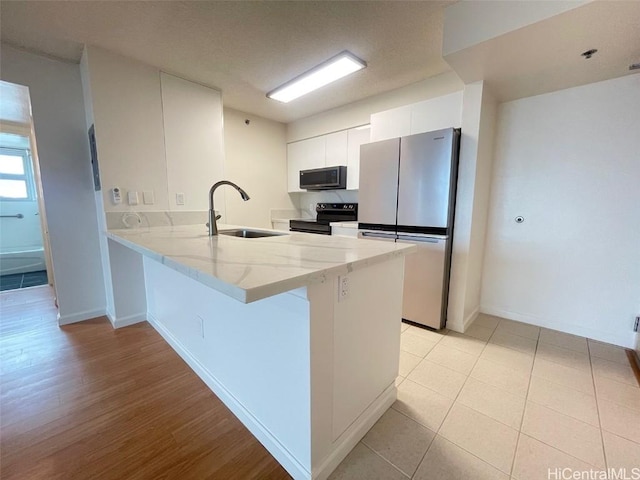 kitchen featuring sink, stainless steel fridge, white cabinetry, electric range, and kitchen peninsula