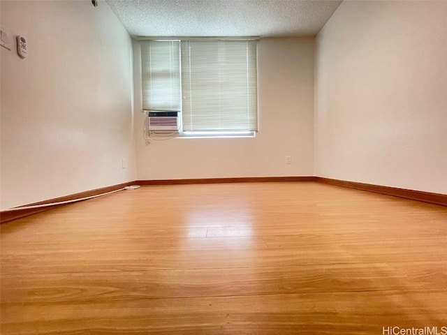 spare room featuring cooling unit, a textured ceiling, and light wood-type flooring