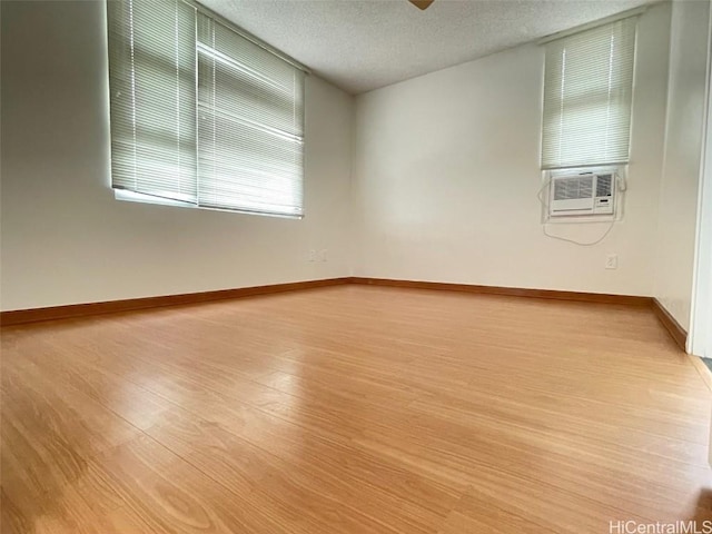 empty room featuring cooling unit, ceiling fan, a textured ceiling, and light wood-type flooring