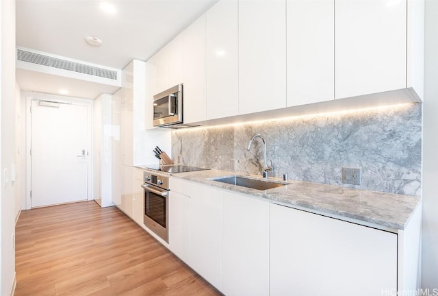 kitchen featuring sink, light hardwood / wood-style flooring, stainless steel appliances, decorative backsplash, and white cabinets