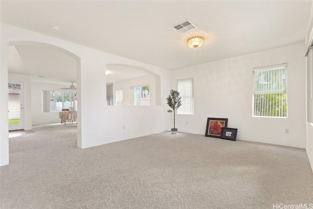 unfurnished room with arched walkways, a ceiling fan, visible vents, and light colored carpet