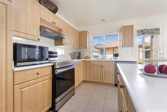 kitchen featuring stainless steel appliances, light countertops, light brown cabinetry, a sink, and wall chimney exhaust hood