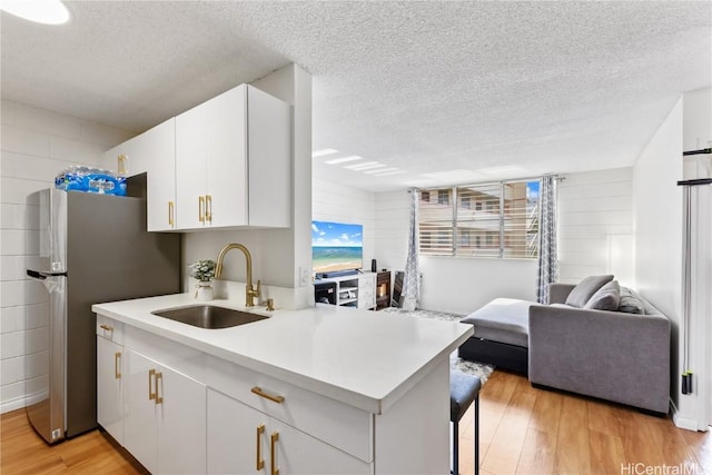 kitchen featuring light wood-style flooring, a sink, open floor plan, freestanding refrigerator, and light countertops