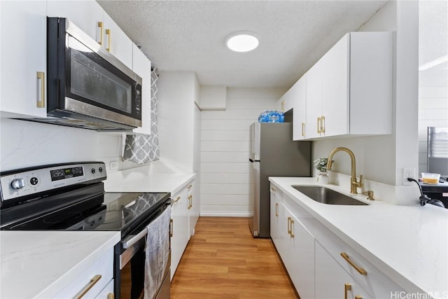 kitchen with a sink, a textured ceiling, stainless steel appliances, light wood-style floors, and white cabinets