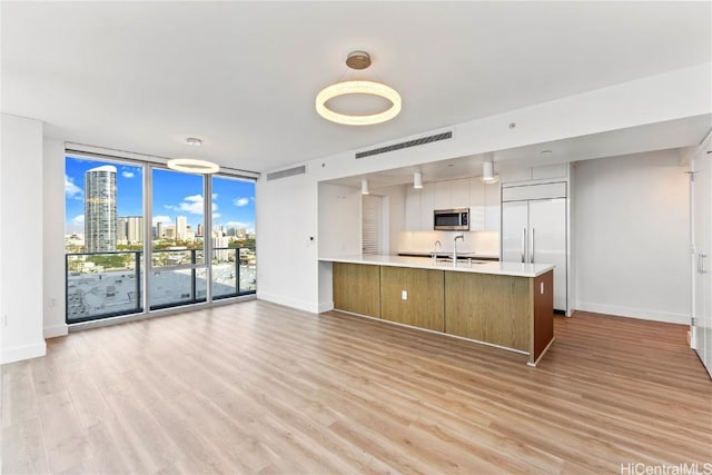 kitchen with appliances with stainless steel finishes, sink, a wall of windows, light hardwood / wood-style floors, and kitchen peninsula