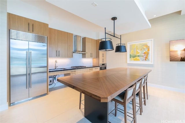 kitchen featuring dark countertops, appliances with stainless steel finishes, wall chimney range hood, pendant lighting, and a sink