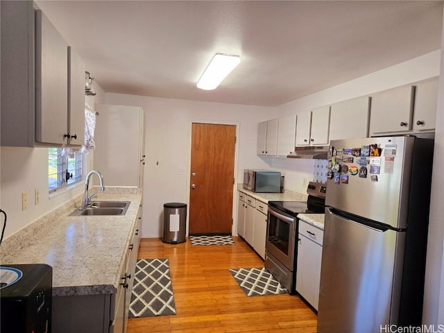 kitchen with sink, stainless steel appliances, light stone countertops, and light wood-type flooring