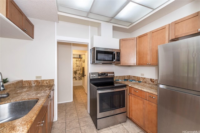 1020 Aoloa Pl Unit 109B, Kailua, HI 96734 - kitchen featuring light stone counters, stainless steel appliances, a sink, light tile patterned flooring, and brown cabinetry