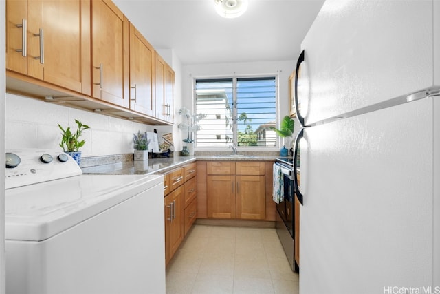 kitchen with brown cabinets, stainless steel electric range oven, freestanding refrigerator, a sink, and washer / dryer