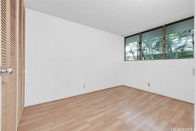 unfurnished room with light wood-style floors, concrete block wall, and a textured ceiling