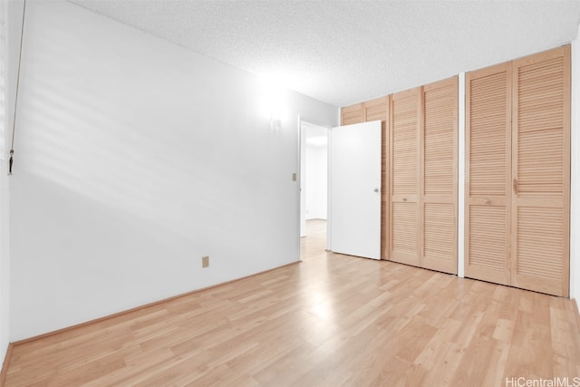 unfurnished bedroom with light wood-style flooring, a textured ceiling, and two closets