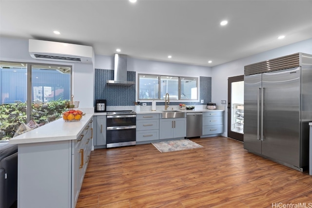 kitchen featuring sink, a wall mounted AC, kitchen peninsula, stainless steel appliances, and wall chimney range hood