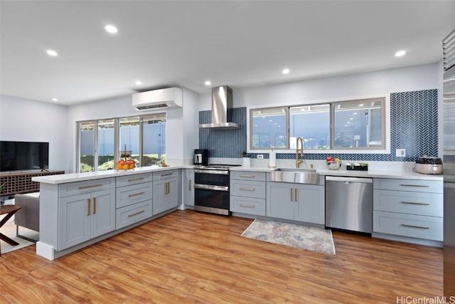 kitchen with appliances with stainless steel finishes, sink, gray cabinetry, a wall unit AC, and wall chimney exhaust hood