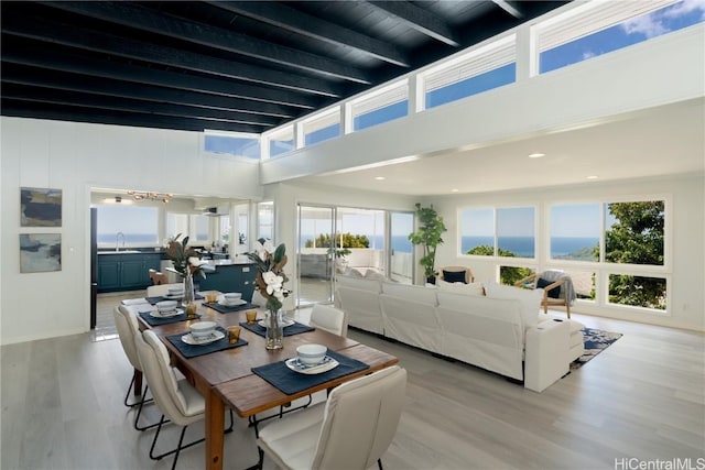 dining area featuring sink, beam ceiling, a water view, and light wood-type flooring