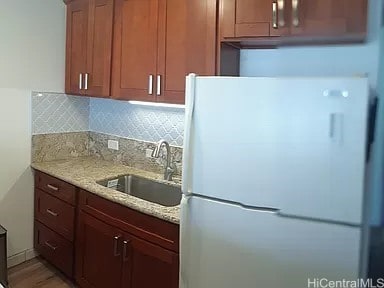 kitchen featuring sink, tasteful backsplash, light stone counters, light hardwood / wood-style flooring, and white refrigerator