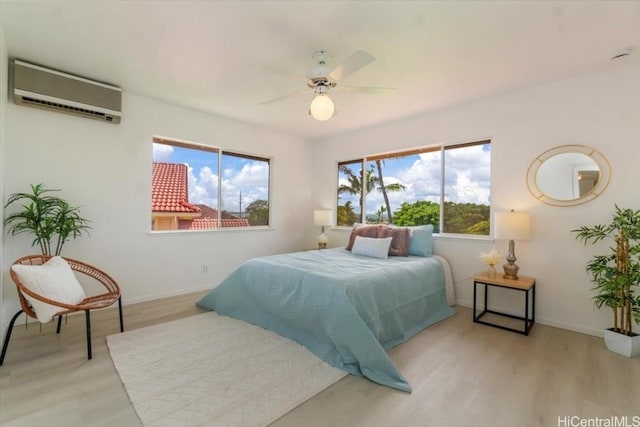 bedroom featuring ceiling fan, a wall unit AC, and light hardwood / wood-style flooring