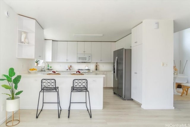 kitchen featuring white cabinets, a kitchen bar, kitchen peninsula, stainless steel refrigerator with ice dispenser, and light wood-type flooring