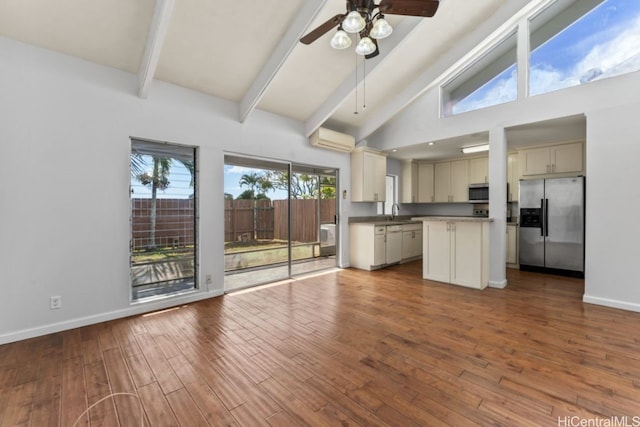 kitchen featuring hardwood / wood-style floors, beam ceiling, stainless steel appliances, cream cabinets, and a wall unit AC