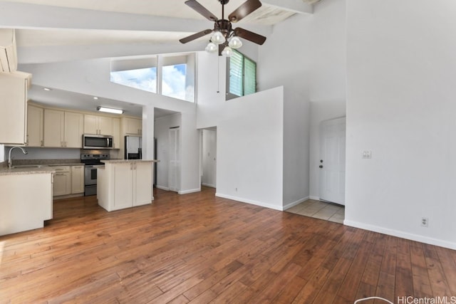 interior space featuring a center island, light wood-type flooring, stainless steel appliances, beam ceiling, and cream cabinets