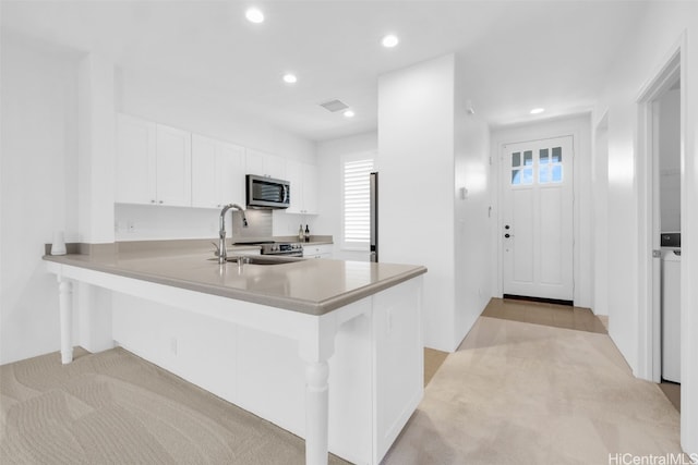 kitchen with appliances with stainless steel finishes, sink, white cabinets, a kitchen breakfast bar, and kitchen peninsula