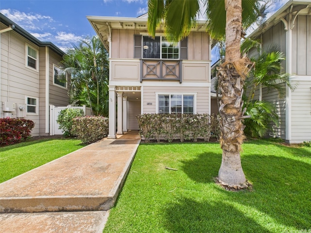 view of property featuring board and batten siding, fence, a front lawn, and a balcony
