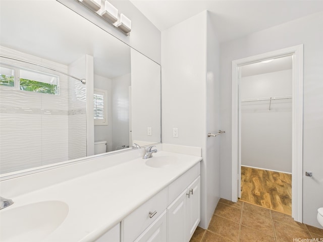 bathroom with double vanity, a tile shower, a sink, and toilet