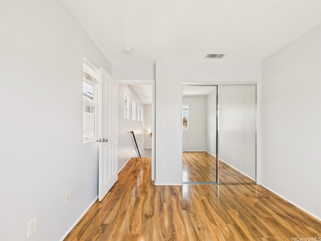 unfurnished bedroom with baseboards, wood finished floors, a closet, and visible vents