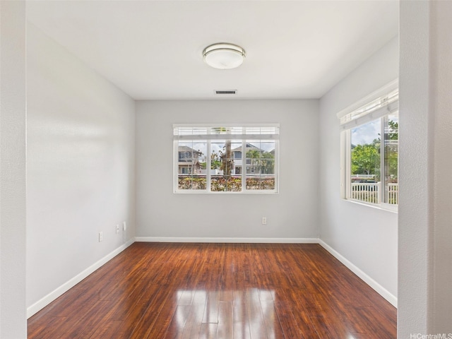 spare room featuring wood-type flooring, a wealth of natural light, and baseboards