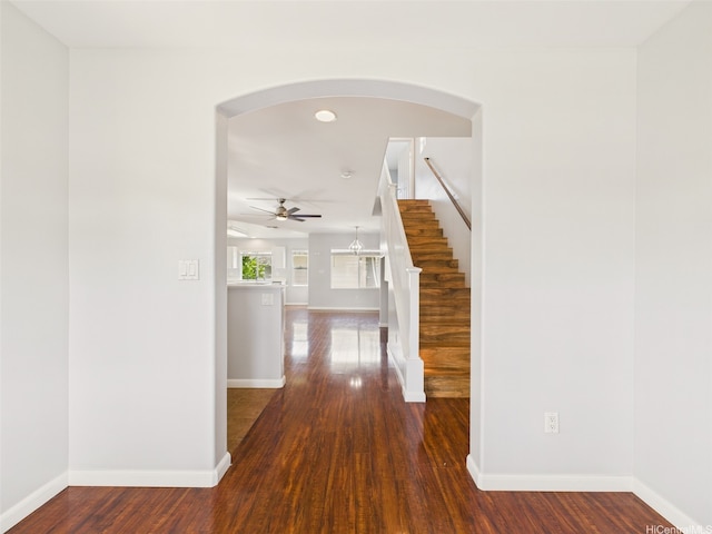 hallway with arched walkways, stairway, baseboards, and dark wood finished floors