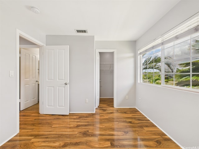 unfurnished bedroom with a closet, baseboards, a walk in closet, visible vents, and wood finished floors
