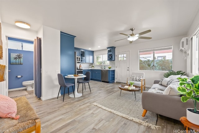 living room featuring a wall mounted air conditioner, sink, ceiling fan, and light wood-type flooring