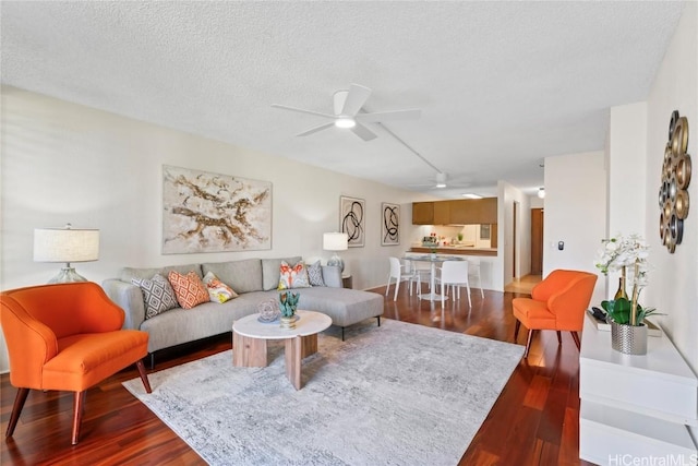 living area with dark wood-type flooring, ceiling fan, and a textured ceiling