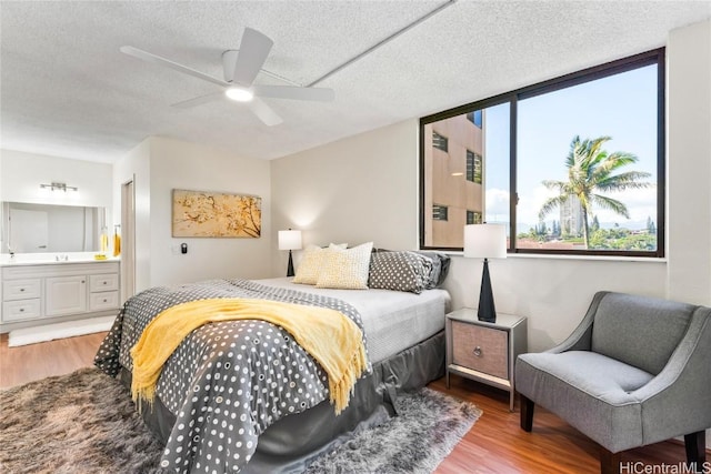 bedroom featuring a ceiling fan, connected bathroom, a textured ceiling, and wood finished floors