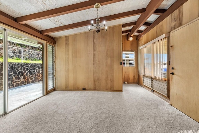 carpeted spare room with an inviting chandelier, beam ceiling, a healthy amount of sunlight, and wood walls