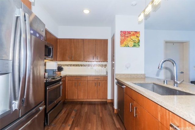 kitchen with appliances with stainless steel finishes, dark hardwood / wood-style floors, sink, decorative backsplash, and light stone counters