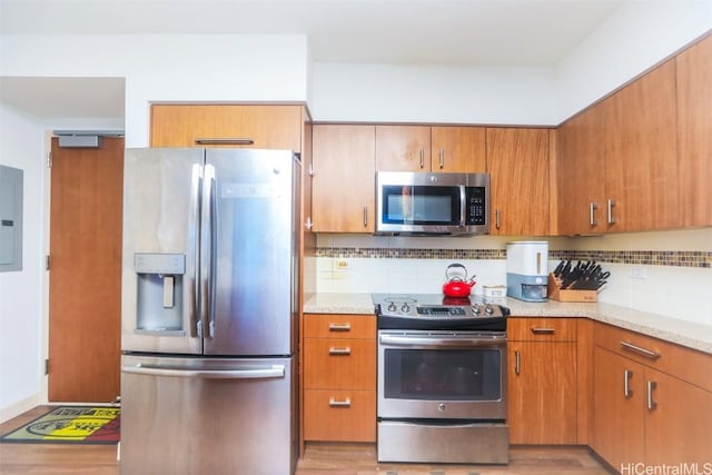 kitchen with light stone counters, tasteful backsplash, light hardwood / wood-style floors, and appliances with stainless steel finishes