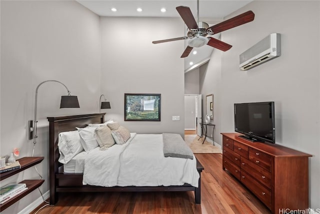 bedroom featuring a wall unit AC, a towering ceiling, light wood-type flooring, and ceiling fan