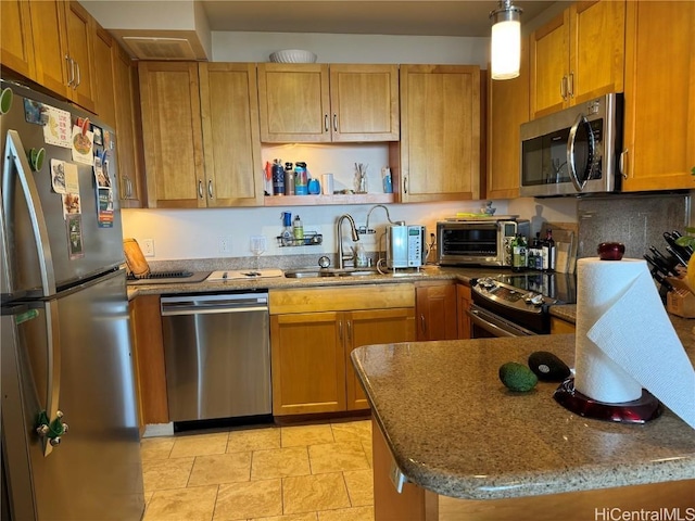 kitchen with appliances with stainless steel finishes, sink, dark stone counters, hanging light fixtures, and kitchen peninsula