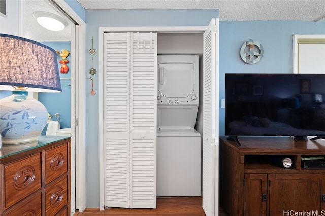 clothes washing area with stacked washer / dryer, hardwood / wood-style flooring, and a textured ceiling