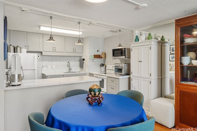 kitchen with pendant lighting, sink, white cabinets, kitchen peninsula, and white appliances