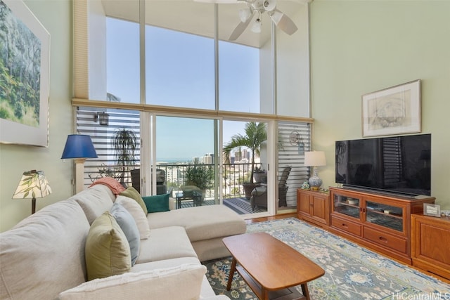 living room with ceiling fan, a wall of windows, and a high ceiling