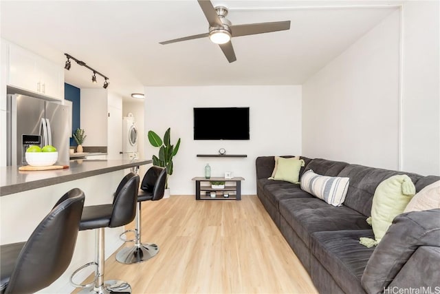 living room with stacked washer and dryer, light hardwood / wood-style flooring, rail lighting, and ceiling fan