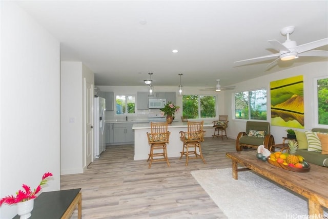 kitchen featuring a kitchen bar, gray cabinets, white appliances, a healthy amount of sunlight, and light hardwood / wood-style floors