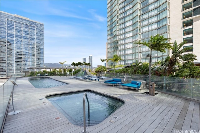 view of pool with a community hot tub, fence, and a view of city