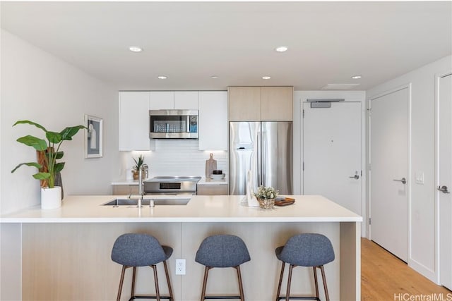 kitchen featuring white cabinetry, light countertops, appliances with stainless steel finishes, modern cabinets, and a kitchen bar