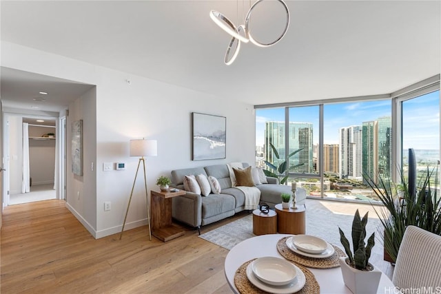 living room featuring light wood-type flooring, a view of city, baseboards, and a wall of windows